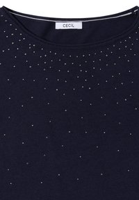 Marineblaues Oberteil mit rundem Ausschnitt, verziert mit verstreuten silbernen Nieten für zusätzliche Textur. Das Etikett trägt die Aufschrift "CECIL."