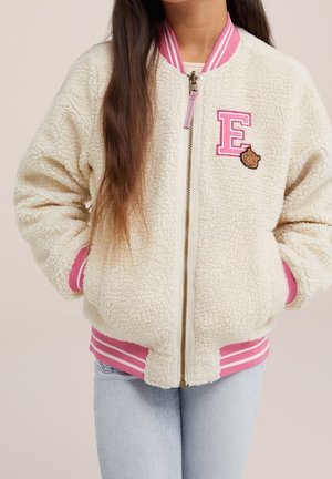 Barn iført creme sherpa-jakke med pinkstribet krave, manchetter og kant, frontlynlås, pink bogstav E-patch og lille tigeransigtsmærke.