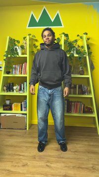 Svart huvtröja med en framficka, jeans i denim med en blekt finish och svarta skor, stående i ett färgglatt rum med hyllor.