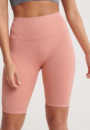 Shorts de vélo roses taille haute avec une texture lisse, présentant un logo imprimé sur le côté et un design ajusté, adaptés à une utilisation sportive.