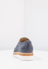Scarpa in pelle blu con design perforato, suola intermedia in sughero, suola esterna in gomma bianca e forma arrotondata. Texture liscia con cuciture a contrasto.