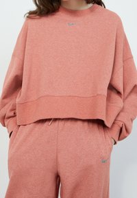 Light coral cropped sweatshirt with oversized fit, ribbed cuffs, and Nike logo in silver at the neckline, paired with matching joggers.
