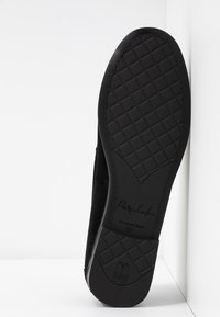 Mocassin en daim noir avec une semelle en caoutchouc texturé, arborant un motif en diamant et un logo en relief au dos. Taille 37.