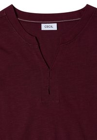 Encolure de chemise marron avec une petite découpe en V et trois coutures horizontales sous le col, avec une étiquette blanche indiquant CECIL.