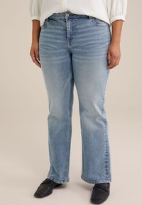 Světle modré džíny z denimu s rovnými nohavicemi, klasickým designem pěti kapes a jemným vyblednutím. Nohou s černými botami.