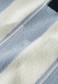 Sinine ja valge triibuline kangas, millel on tekstureeritud pind, kus vahelduvad laiad ja kitsad triibud, peamiselt pehmest villa sarnast materjalist.