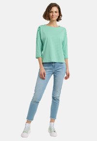 Hellgrünes gestreiftes Langarmoberteil mit weitem Halsauschnitt und Dreiviertelärmeln, kombiniert mit hellblauen cropped Jeans und hellgrünen High-Top-Sneakern.