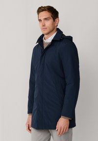 Marineblauer, wasserabweisender Mantel mit abnehmbarem Kapuzenhut, mit Reißverschluss vorne und Seitentaschen. Besitzt eine glatte Textur und klare Linien.