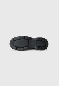 Suela de zapato de goma negra con una superficie texturizada, detalles de logo y patrones de tracción pronunciados para una mejor control de la tracción.