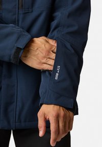 Navy waterproof jacket with a textured finish. Features a zippered pocket and velcro cuff adjustments. "STX 8000" label on the sleeve.