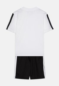 Vit t-shirt med svarta axelränder, matchad med svarta shorts som har vita sidostripes. Tillverkad av mjukt, andningsbart tyg.