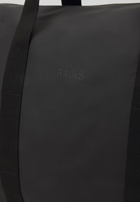 Sac de sport noir imperméable avec une finition texturée, doté de poignées en sangle noire robustes et du logo embossé "RAINS" à l'avant.