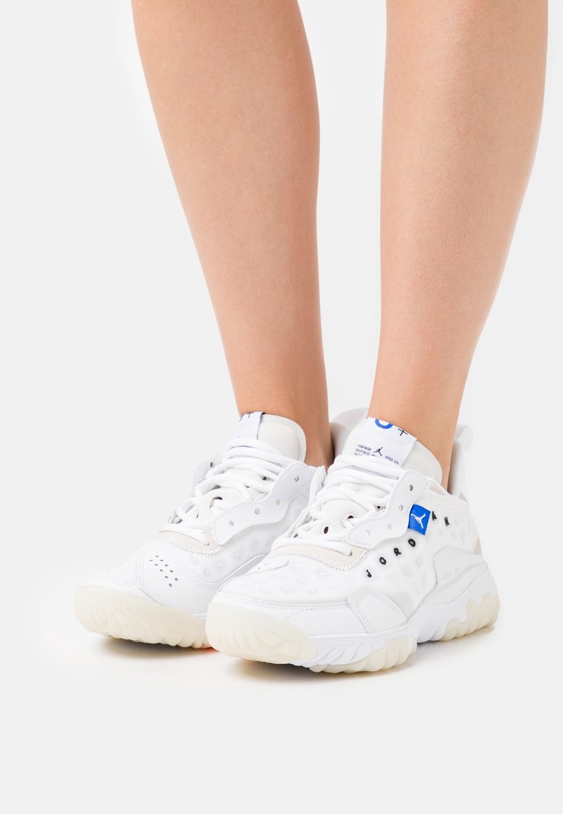 Vita atletiska skor med texturerad ovandel, vadderad krage, blå logotypdetalj och tjock, krämfärgad gummisula.