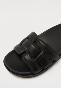 Sandale mule en cuir noir avec deux brides superposées, texture lisse et semelle plate. Design simple sans motifs ni accents supplémentaires.