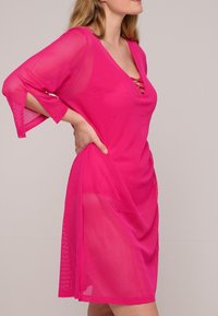 Geweven roze mesh cover-up jurk met een V-hals, driekwart mouwen en een strikdetail bij de hals. Lichtgewicht, losvallend ontwerp.