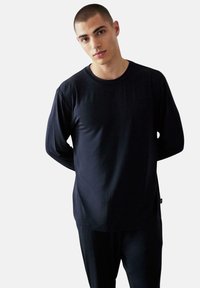 Námořnická modrá košile s dlouhým rukávem vyrobená z hladkého materiálu, s kulatým výstřihem a volným střihem. Minimalistický design bez vzorů.