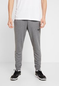Šedé jogger kalhoty vyrobené z měkké tkaniny s tapered střihem, s malým černým logem Nike na stehně a elastickými manžetami na kotnících.