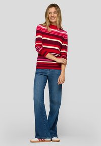 Langärmliger Pullover mit rot-rosa Streifen, kombiniert mit blauen, ausgestellten Jeans und weißen Turnschuhen mit roten und blauen Akzenten.