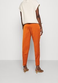 Oranje taps toelopende broek met een gladde textuur, gecombineerd met een crèmekleurige gebreide top met een losse pasvorm en kapmouwen.