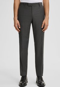 Uomo con pantaloni eleganti a righe grigio scuro e scarpe eleganti in pelle nere su uno sfondo grigio chiaro.