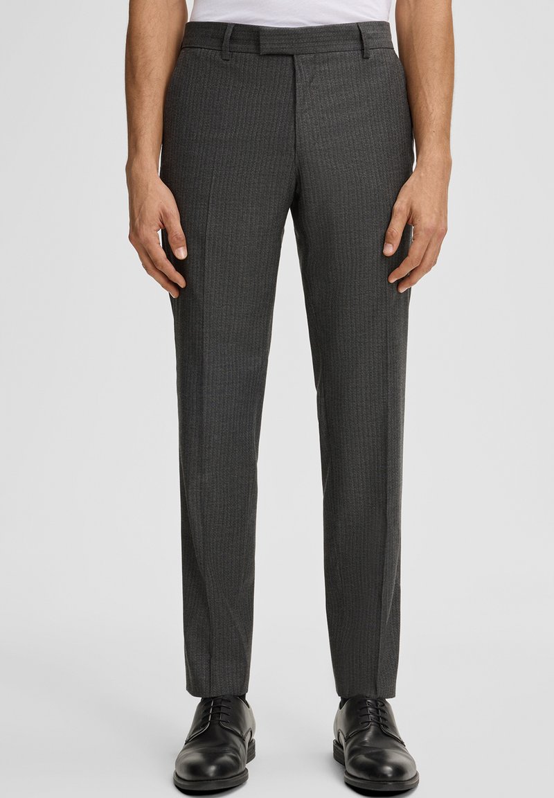 Uomo con pantaloni eleganti a righe grigio scuro e scarpe eleganti in pelle nere su uno sfondo grigio chiaro.