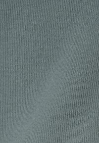 Tejido texturizado y acanalado en un color verde azulado apagado, que presenta finas líneas paralelas para una superficie táctil y suave.