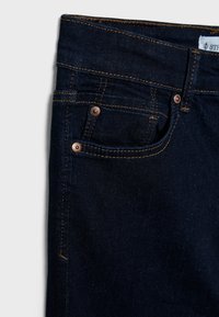 Dark blue denim jeans with copper-toned rivets, exposed stitching, and a front pocket. Smooth texture and classic fit design.