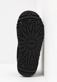 Svart gummisula med texturerat mönster, med en cirkulär logotyp och triangulära mönster; slät yta med en lätt glans.
