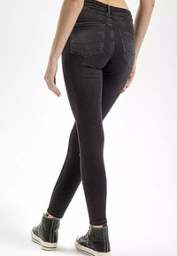 Czarne skinny jeansy z wysokim stanem i tylnymi kieszeniami, o gładkiej fakturze i dopasowanym kroju, w zestawieniu z czarnymi sneakersami typu high-top.