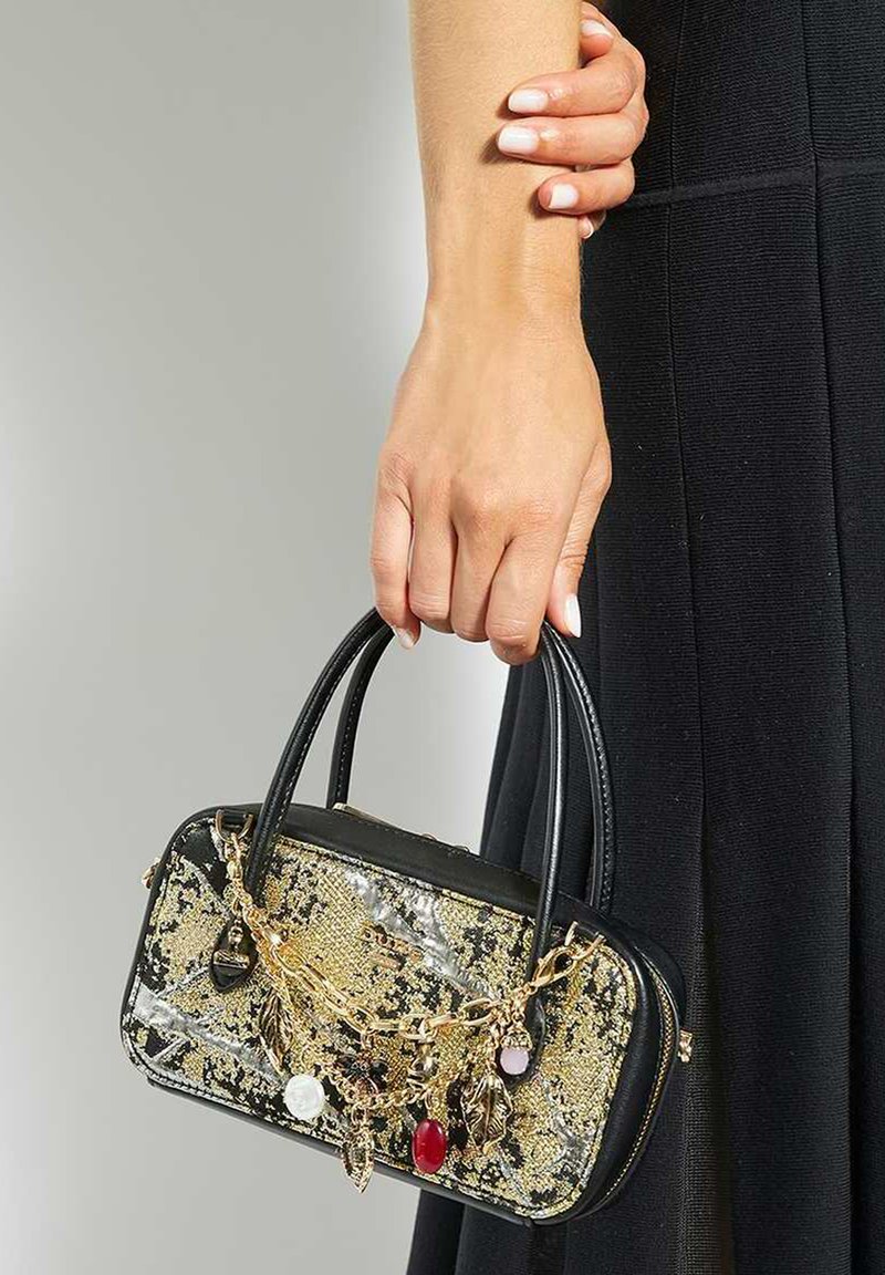 Black handbag with gold and silver snake print, featuring a chain with decorative charms, small handles, and a glossy texture.