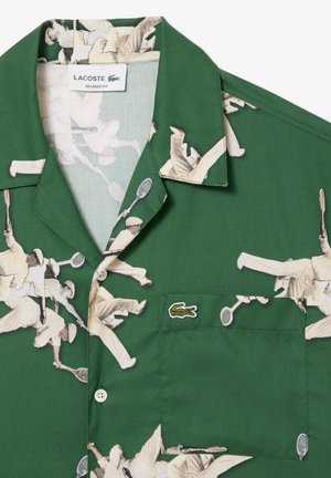 Chemise verte à manches courtes avec un imprimé de joueur de tennis rétro, coupe décontractée, poche poitrine et un petit logo brodé sur la poche.