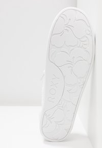 Semelle de chaussure blanche avec des motifs floraux et le mot ROXY embossé au centre, présenté à la verticale sur fond blanc.