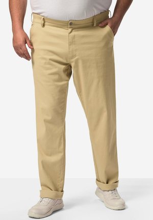 Pantalons en coton beige à coupe droite, avec des poches latérales, une fermeture à bouton, des poignets retroussés, et associés à des baskets de couleur claire.