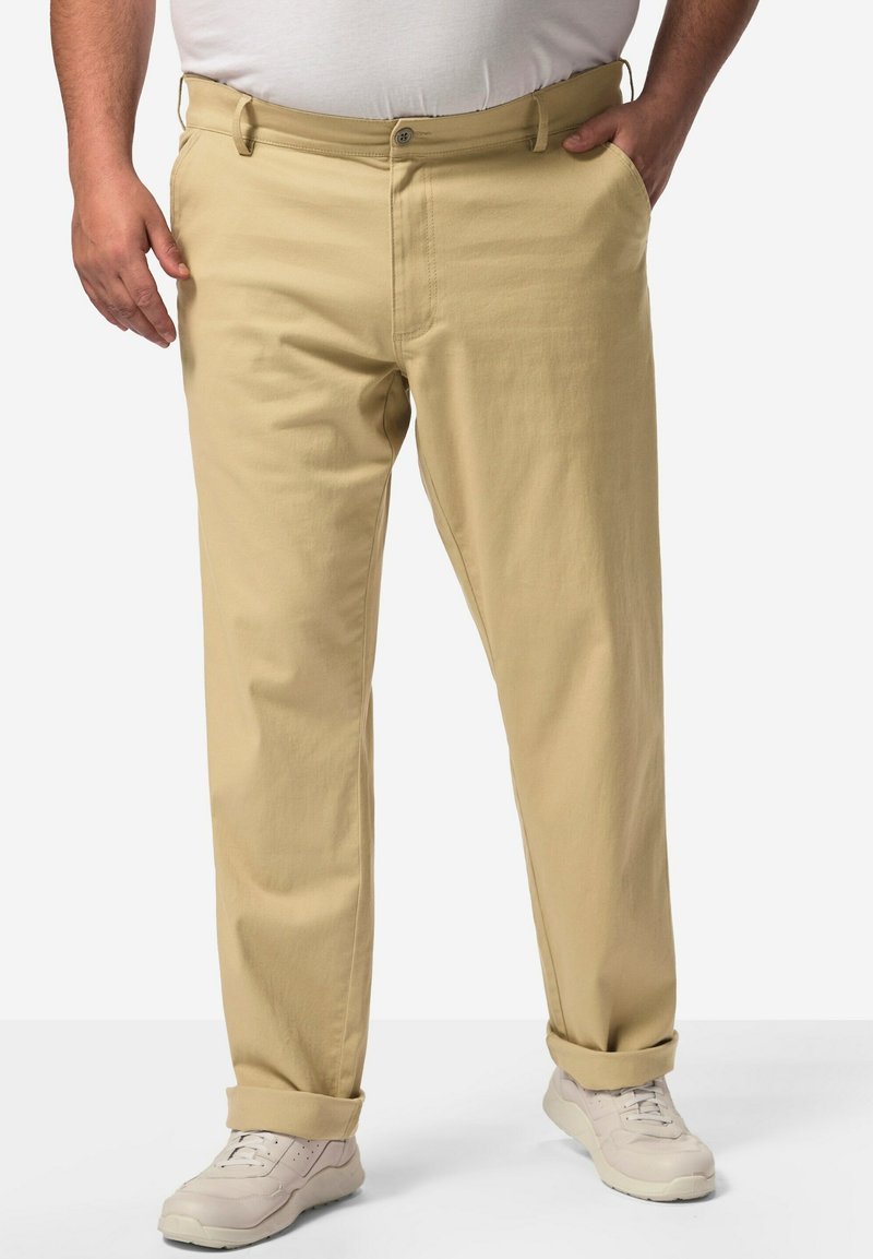 Pantaloni di cotone beige con taglio dritto, dotati di tasche laterali, chiusura con bottone, risvolti e abbinati a sneaker di colore chiaro.
