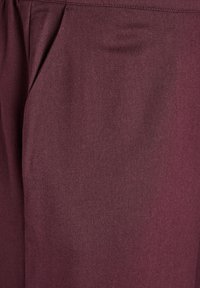 Tissu bourgogne avec une texture lisse et un subtil éclat, présentant des plis à l'avant et des poches latérales pour une fonctionnalité accrue.