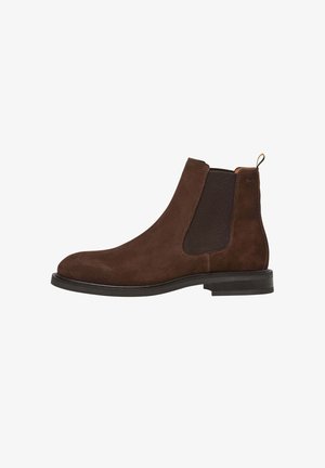 Bottines Chelsea en daim marron avec des panneaux élastiques sur les côtés, bout rond et une languette. Elles présentent une semelle noire plate et des coutures contrastées.