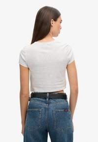 Camiseta gris cortada de manga corta, con un sencillo cuello redondo, combinada con unos jeans de mezclilla azul deslavado de tiro alto y un cinturón negro.