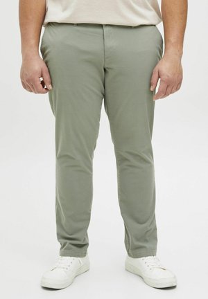 Chinos de algodón verde claro con corte slim, que cuentan con bolsillos laterales y una textura lisa, combinados con zapatillas blancas.