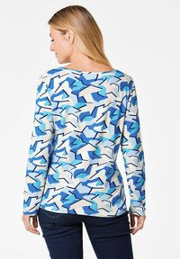 Langärmliges Oberteil mit einem blauen und weißen abstrakten geometrischen Muster. Hergestellt aus einem leichten Stoff mit lockerer Passform und weitem Ausschnitt.