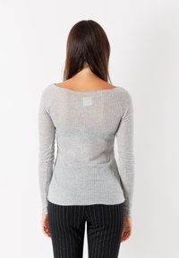 Maglietta grigia a maniche lunghe con texture a coste, scollo ampio e design aderente. Indossata con pantaloni neri a righe, che mostrano la vista posteriore.