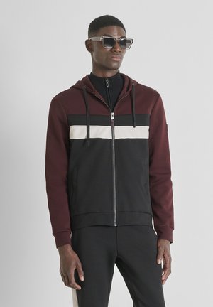 Bordeauxrot und schwarze Kapuzenjacke mit kontrastierenden horizontalen Streifen in Weiß und Beige. Sie verfügt über verstellbare Kordeln und Seitentaschen.