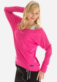 Fuchsia roze langemouwtop met een relaxed fit, off-the-shoulder ontwerp en grijze laag eronder, met een merklabel aan de onderkant.