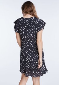 Robe noire à pois blancs avec de courtes manches volantées, ourlet froncé, fermeture à boutons au dos, fabriquée en tissu léger.