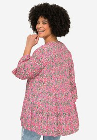 Blouse florale rose avec des manches bouffantes, un ourlet volanté et un tissu léger. Présente de petits motifs de fleurs multicolores sur l'ensemble.