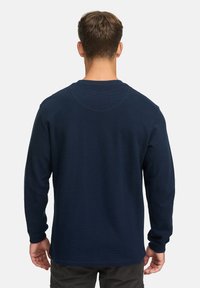 Marineblå langærmet skjorte lavet af tekstureret stof, med en ribbet rund hals og tætsiddende manchetter. Bagsiden fremhæver et ensfarvet design.