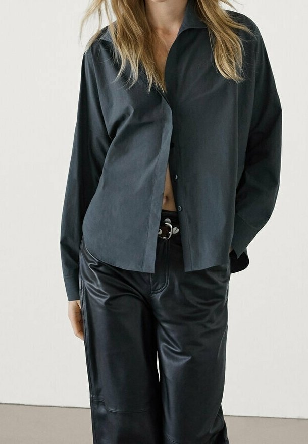 Chemise noire ample en tissu lisse, dotée d'un col et d'une fermeture à boutons, associée à un pantalon large en cuir noir brillant.