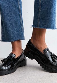 Svarta lackläder loafers med dekorativ kvast, med en kraftig gummisula och en slät, glansig yta, matchade med fransiga denim.