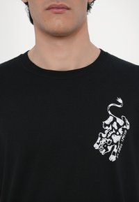 Black cotton T-shirt with short sleeves. Features a white graphic of a cow with the text "PS PAUL SMITH" in a modern font on the chest.