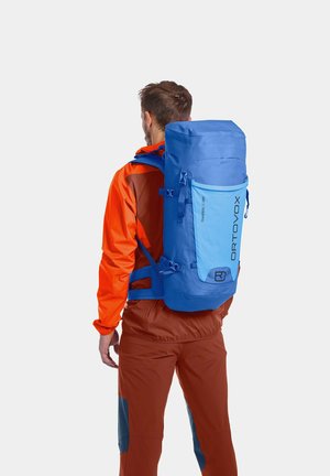 Blauer und hellblauer Rucksack mit Rolltop-Design, verstellbaren Trägern und einer Fronttasche; strapazierfähiges Material, das sich für den Einsatz im Freien eignet.