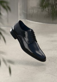 Scarpa da uomo in pelle nera con finitura lucida, punta affusolata e design classico con lacci. Presenta una superficie liscia e un tacco leggero.